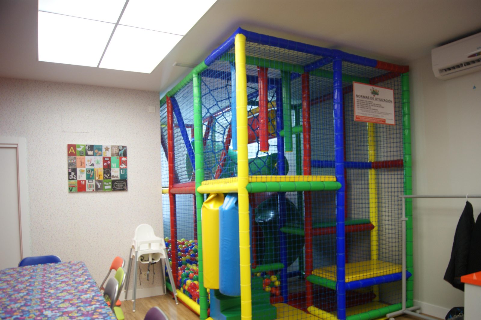 La zona infantil: una estructura de juegos con redes, tubos de colores y tobogán, y detrás el comedor