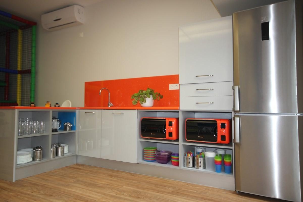 El office, con la cocina naranja, la nevera y los microondas